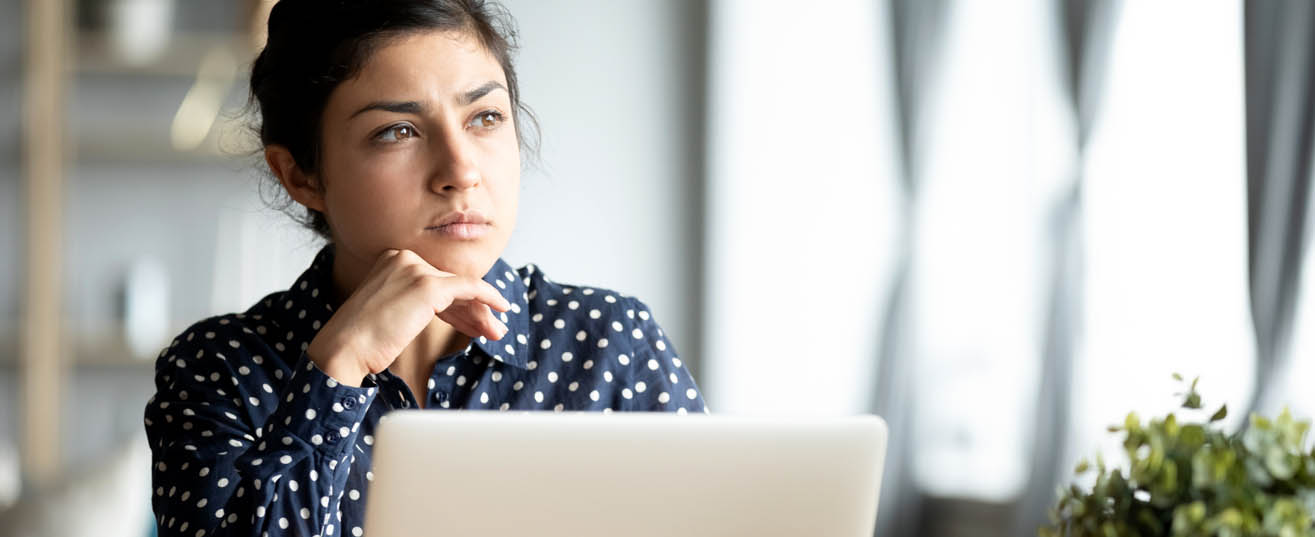 Woman sitting in front of laptop, thinking.